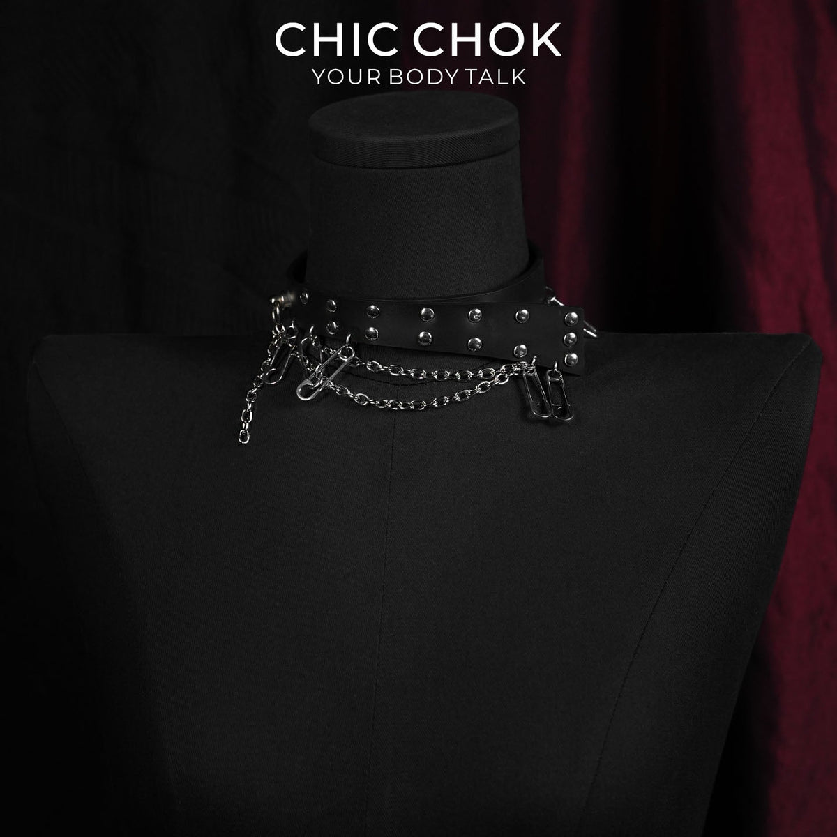 Black strap choker with rivets, safety pins, and hanging chains on a necklace display