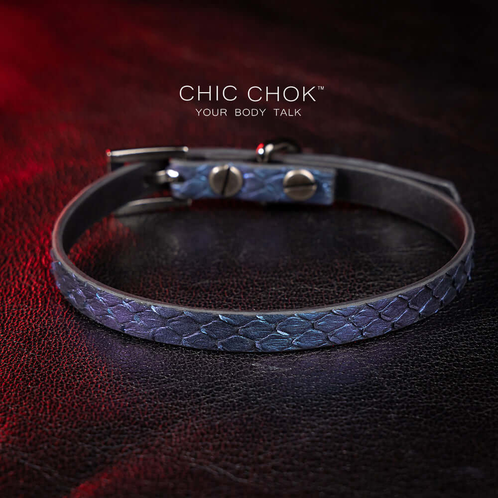 chicchok salome choker featuring a textured midnight blue snakeskin design with a silver buckle clasp, captured against a dark leather background illuminated by red highlights. Perfect for gothic and elegant fashion enthusiasts.