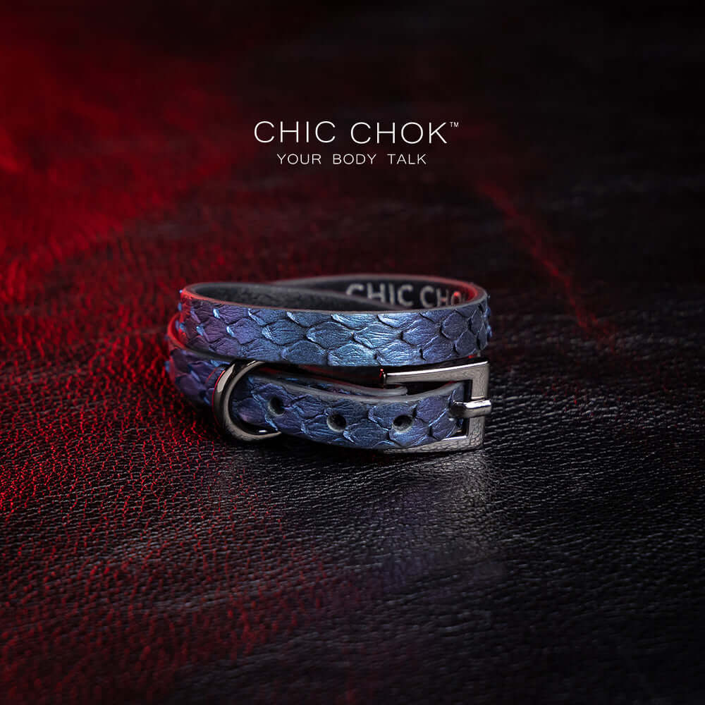 chicchok salome choker featuring a textured midnight blue snakeskin design with a silver buckle clasp, captured against a dark leather background illuminated by red highlights. Perfect for gothic and elegant fashion enthusiasts.