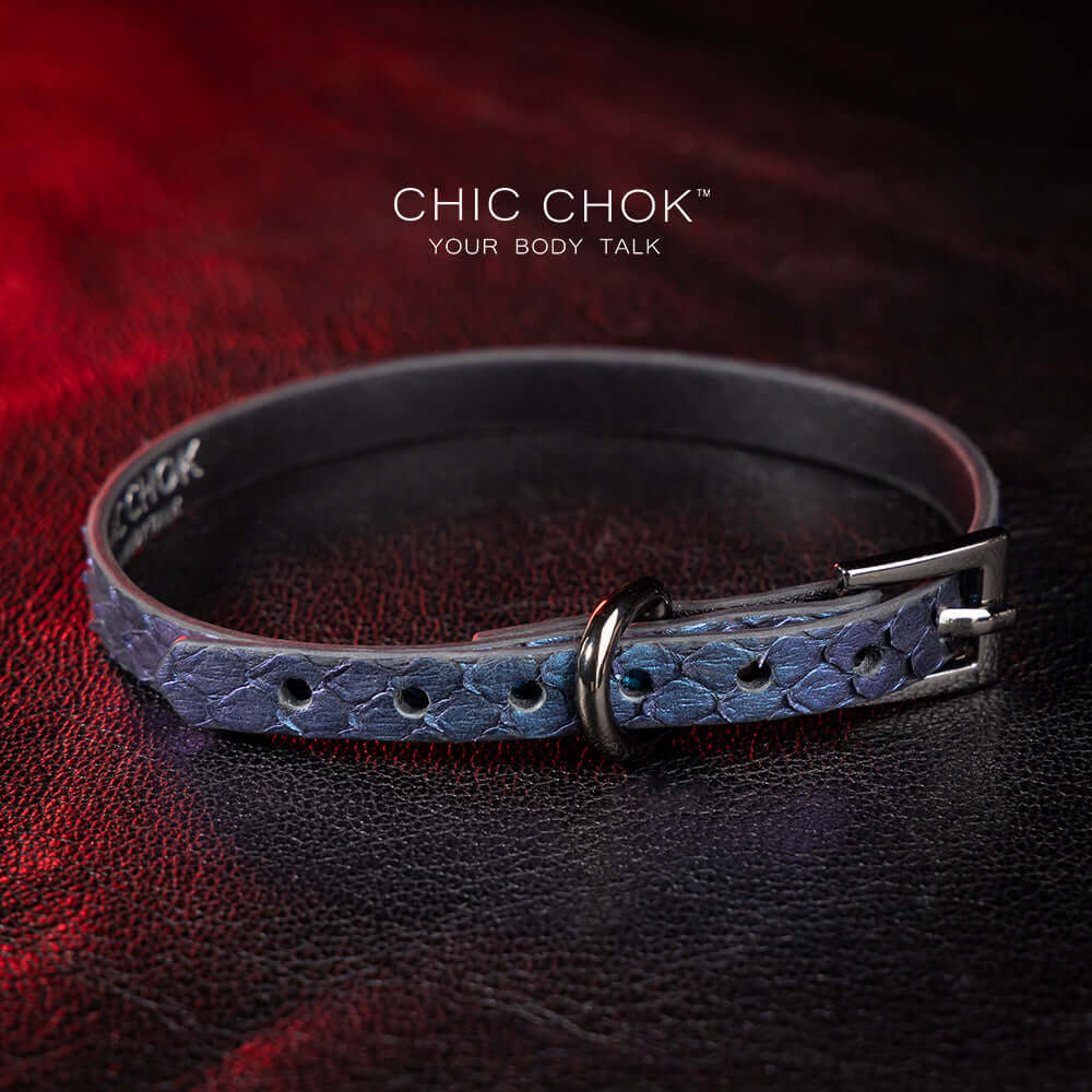 chicchok salome choker featuring a textured midnight blue snakeskin design with a silver buckle clasp, captured against a dark leather background illuminated by red highlights. Perfect for gothic and elegant fashion enthusiasts.