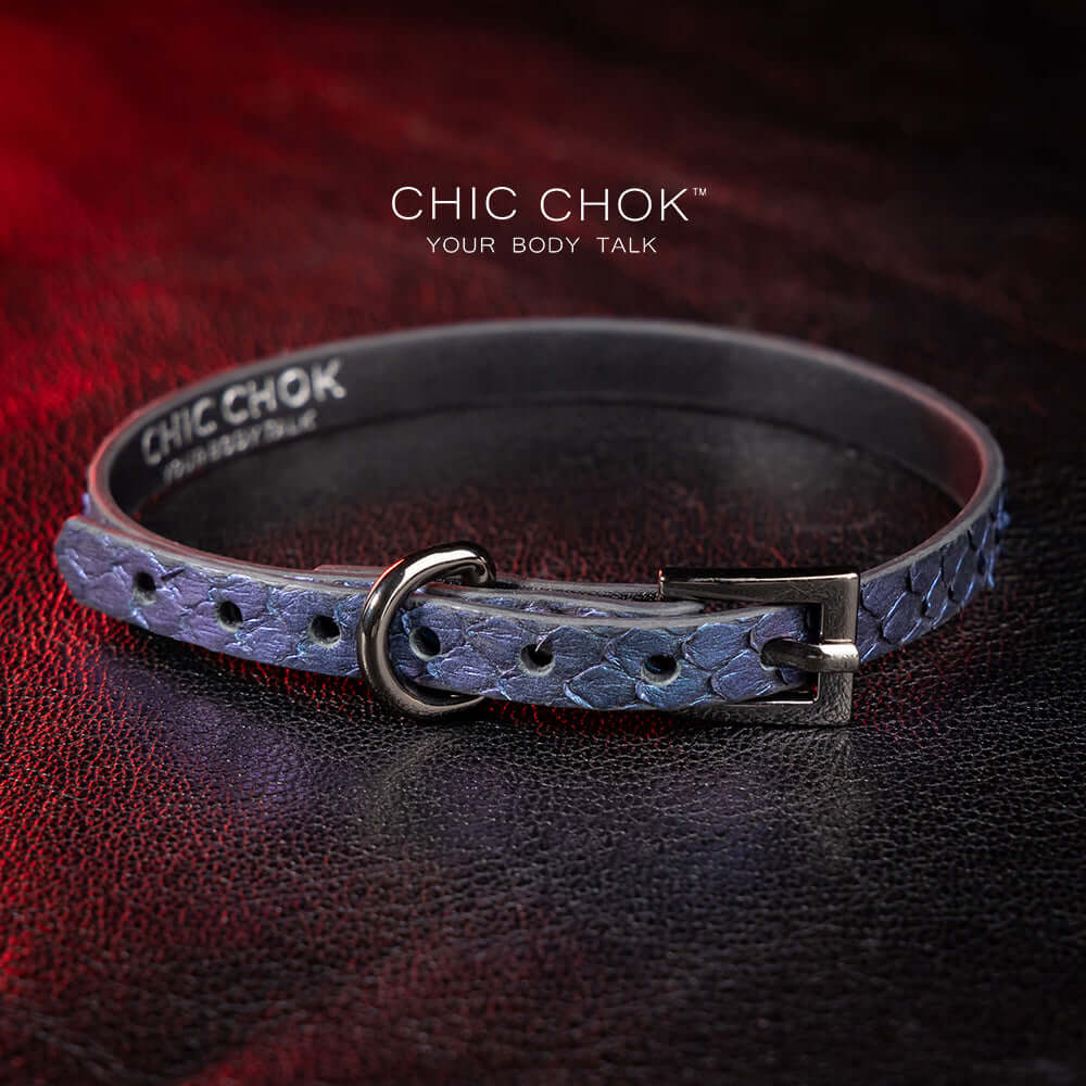 chicchok salome choker featuring a textured midnight blue snakeskin design with a silver buckle clasp, captured against a dark leather background illuminated by red highlights. Perfect for gothic and elegant fashion enthusiasts.