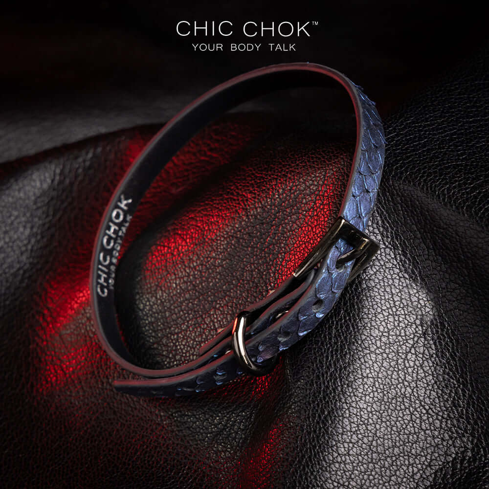 chicchok salome choker featuring a textured midnight blue snakeskin design with a silver buckle clasp, captured against a dark leather background illuminated by red highlights. Perfect for gothic and elegant fashion enthusiasts.