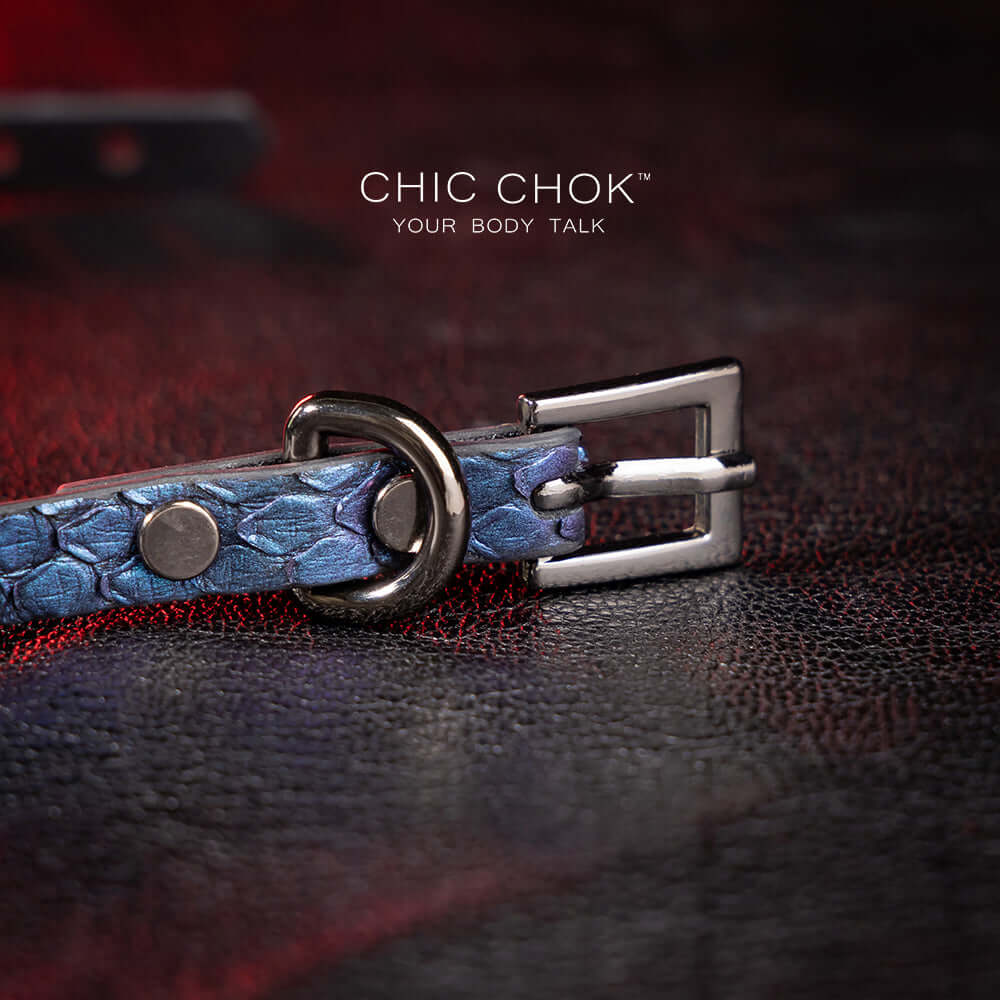chicchok salome choker featuring a textured midnight blue snakeskin design with a silver buckle clasp, captured against a dark leather background illuminated by red highlights. Perfect for gothic and elegant fashion enthusiasts.