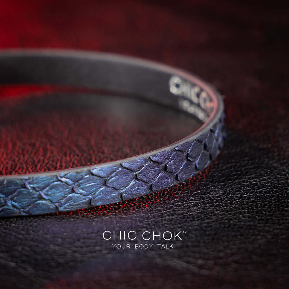 chicchok salome choker featuring a textured midnight blue snakeskin design with a silver buckle clasp, captured against a dark leather background illuminated by red highlights. Perfect for gothic and elegant fashion enthusiasts.